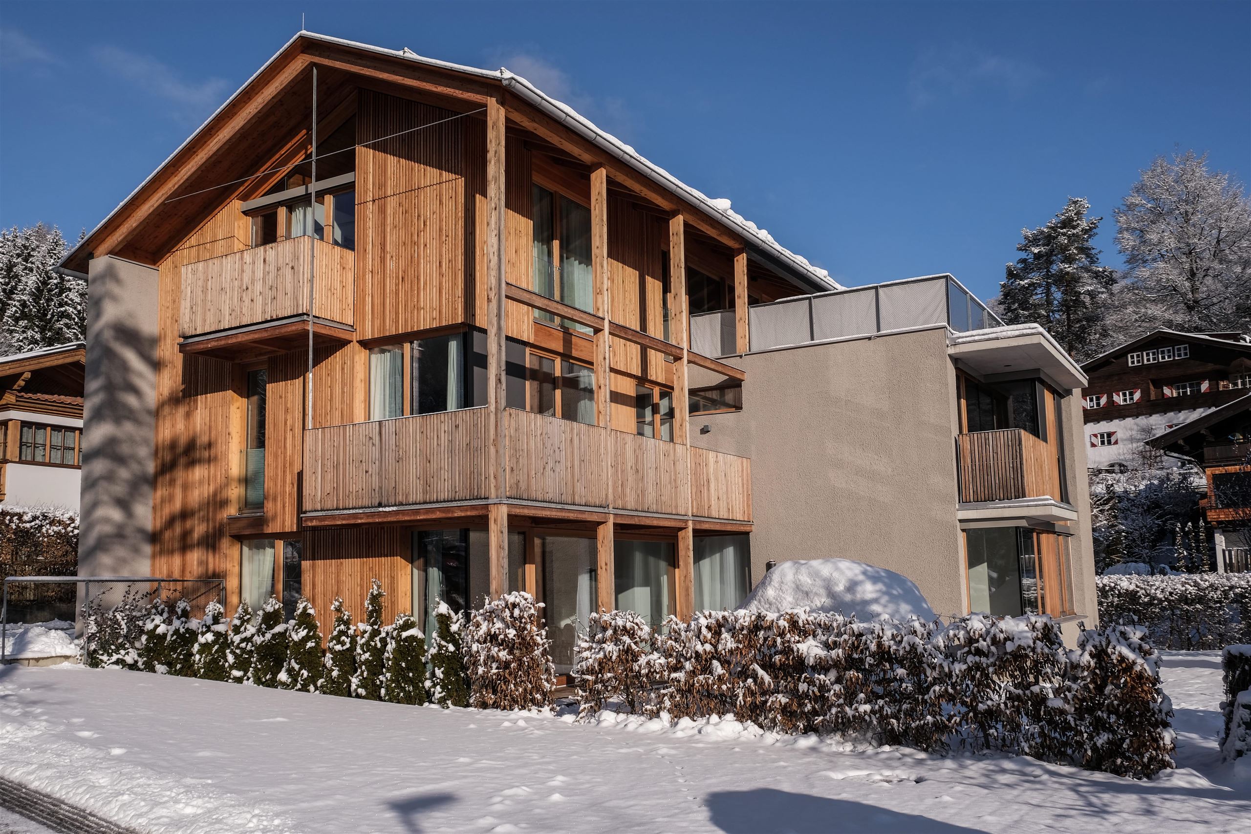 Ein modernes, holzverkleidetes Gebäude in einer verschneiten Umgebung. Der Winterzauber wird durch den klaren Himmel und die schneebedeckte Landschaft verstärkt.