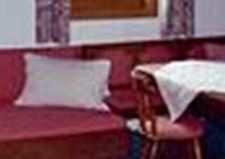 Ein gemütlicher Raum mit einer roten Bank, einem Tisch und Stühlen. Die Wände sind mit Fenster und Vorhängen dekoriert.