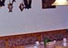 Ein rustikales Esszimmer mit Holztischen und Stühlen. An der Wand hängen Geweihe und es gibt eine gemütliche Feuerstelle.