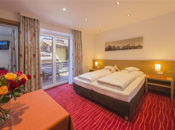 Ein gemütliches Zimmer mit zwei Einzelbetten und einem Tisch. Der Raum hat einen Balkon mit Aussicht und ist hell erleuchtet.