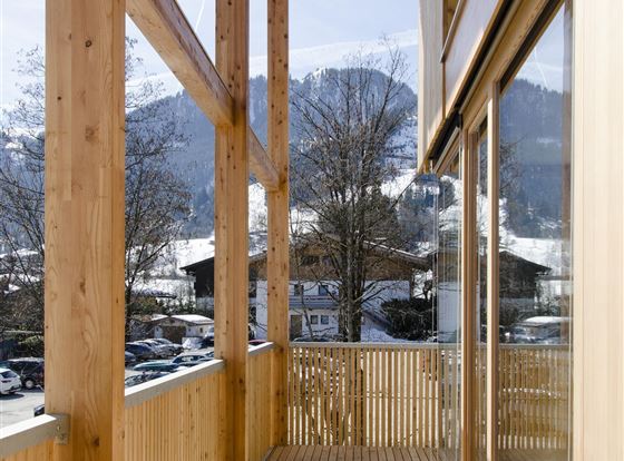 Ein moderner Balkon aus Holz mit panoramichem Blick auf die Berge und eine klare Winterlandschaft. Die großen Fenster lassen viel Licht hereinfahren.
