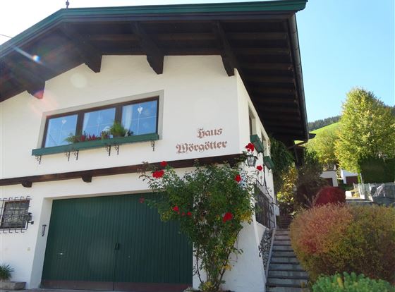 Ein gemütliches Haus mit dem Namen "Haus Wenzel" an einer sonnigen Straße. Abgerundet wird das Bild durch üppige Pflanzen und einen gepflegten Garten.