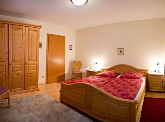 Ein gemütliches Schlafzimmer mit einem großen Bett und roten Kissen. Der Raum ist mit Holzschränken und einem Teppich ausgestattet.