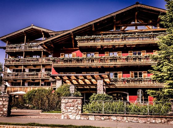 Ein schönes Holzhaus im Alpenstil mit mehreren Balkonen. Umgeben von Bäumen und grünen Pflanzen.