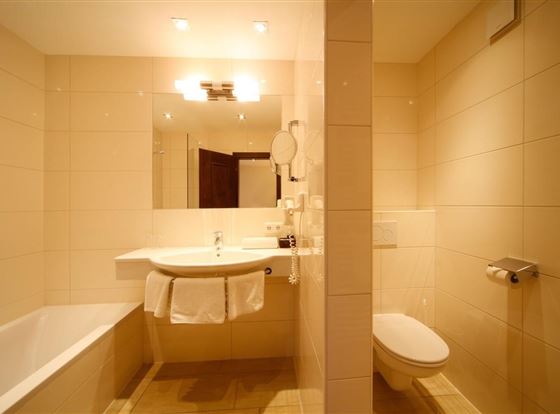 Ein modernes Badezimmer mit einer Badewanne, einem Waschbecken und einer Toilette. Die Wände sind hell und die Beleuchtung ist weich.