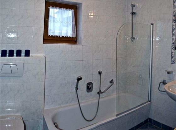 Ein modernes Badezimmer mit einer Badewanne und einer Dusche. Die Wände sind hell gefliest und ein kleines Fenster sorgt für Tageslicht.