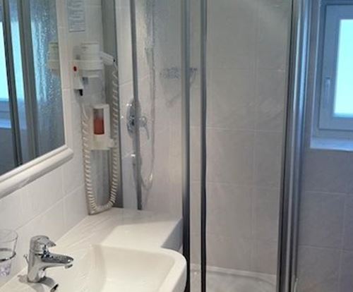 Ein modernes Badezimmer mit einer Dusche und einem Waschbecken. Die Wände sind in Weiß gehalten, und es gibt ein Fenster, das für natürliches Licht sorgt.