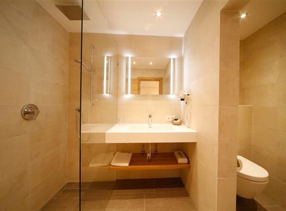 Ein modernes Badezimmer mit hellen Fliesen und eleganter Beleuchtung. Das Waschbecken ist schick und es gibt eine transparente Duschkabine.