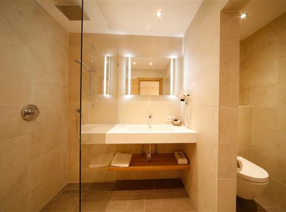 Ein modernes Badezimmer mit einer gläsernen Duschkabine und einem schlichten Waschbecken. Die Wände sind in einem hellen Beigeton gehalten, was eine freundliche Atmosphäre schafft.