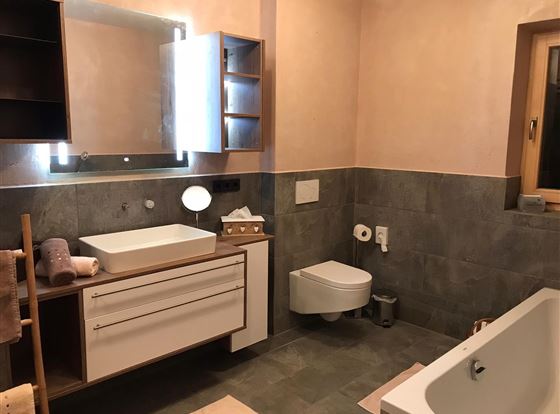 Ein modernes Badezimmer mit einer Badewanne, einem Waschbecken und einem großen Spiegel. Die Wände sind in sanften Farben gehalten und es gibt praktische Ablageflächen.