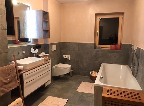 Ein modernes Badezimmer mit einer Badewanne und einem Waschbecken. Die Wände sind in sanften Farben gehalten und es gibt eine große Spiegelfläche.