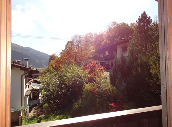 Ein Blick aus einem Fenster auf eine bunte Herbstlandschaft. Bäume und Häuser sind von warmem Licht beleuchtet.