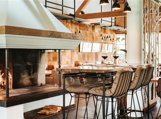 A modern restaurant with an inviting fireplace and stylish bar stools. The space is brightly and cozily designed.