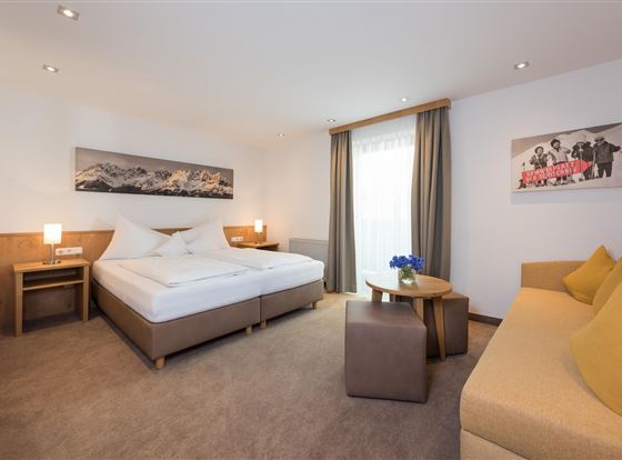 Ein modernes Hotelzimmer mit einem Doppelbett und einem Schlafsofa. Das Zimmer ist hell und freundlich, mit Dekoration an den Wänden.