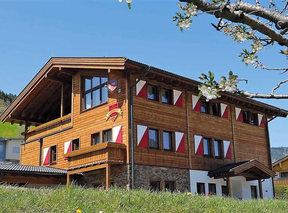 Ein schönes Holzhaus mit bunten Fensterläden und einem gepflegten Garten. Die klare Himmelsfarbe und die umliegende Landschaft verleihen dem Haus eine einladende Atmosphäre.