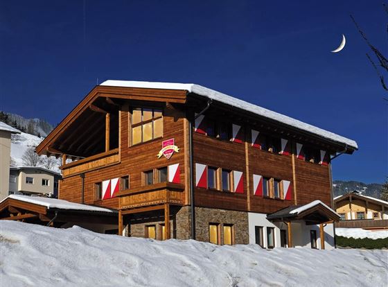 Ein schönes Holzhaus im Winter, umgeben von Schnee. Der Himmel ist klar und der Mond ist sichtbar.
