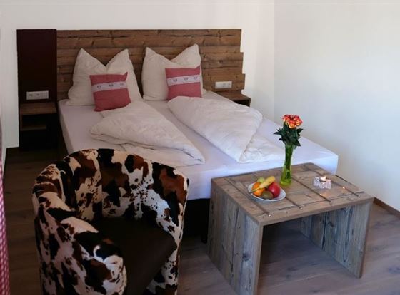 Ein gemütliches Schlafzimmer mit einem Doppelbett und gepolsterten Kissen. Neben dem Bett steht ein Tisch mit frischem Obst und einer Vase mit einer Blume.
