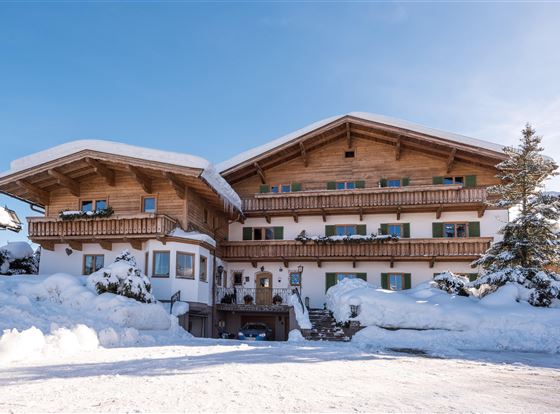 Ein charmantes Holzhaus im Schnee mit einem blauen Himmel. Der Eingang ist einladend und die Umgebung ist winterlich schön.