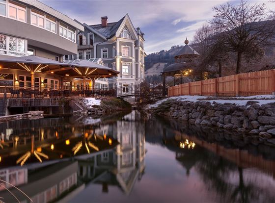 Ein modernes Gebäude am Wasser, umgeben von einer ruhigen Landschaft. Die Beleuchtung reflektiert sich schön im Wasser.