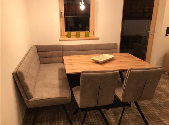 Ein modernes Esszimmer mit einer U-förmigen Bank und einem Holztisch. Die warmen Farben und das gemütliche Ambiente laden zum Verweilen ein.