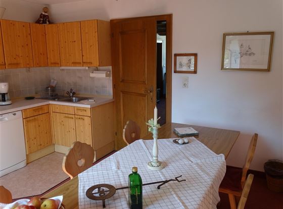 Eine gemütliche Küche mit Holzmöbeln und einem Tisch. Auf dem Tisch stehen Äpfel und eine dekorative Flasche.