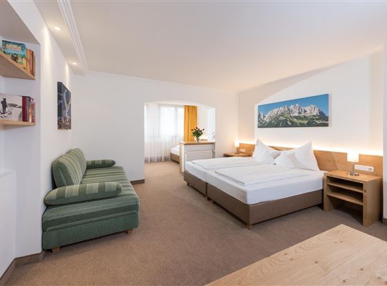 Ein helles Zimmer mit zwei Betten und einem gemütlichen Sofa. Große Fenster sorgen für viel Tageslicht.