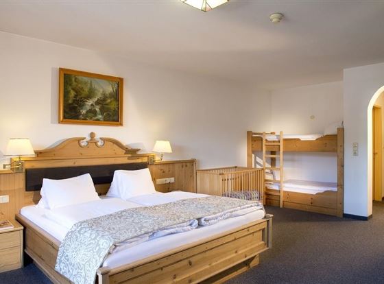 Ein gemütliches Hotelzimmer mit einem Doppelbett und einem Etagenbett. Es gibt Holzmöbel und ein Fenster mit einem schönen Bild an der Wand.