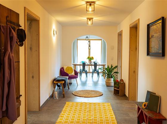 Ein heller Flur mit modernen Lampen und einer gemütlichen Einrichtung. Am Ende des Flurs befindet sich ein Tisch mit Blumen und Stühlen.