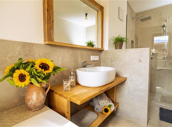 Ein modernes Badezimmer mit Holzregal und einem eleganten Waschbecken. Sonnenblumen und Pflanzen sorgen für eine freundliche Atmosphäre.