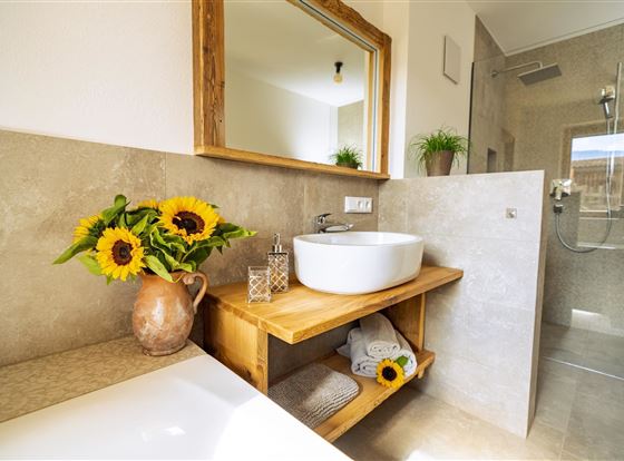 Ein modernes Badezimmer mit einem runden Waschbecken auf einem Holztisch. Sonnenblumen und dekorative Elemente verleihen dem Raum eine freundliche Atmosphäre.