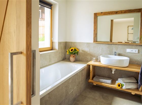 Ein modernes Badezimmer mit einer Badewanne und einer schönen Holzablage. Auf der Ablage stehen frische Sonnenblumen und Handtücher.