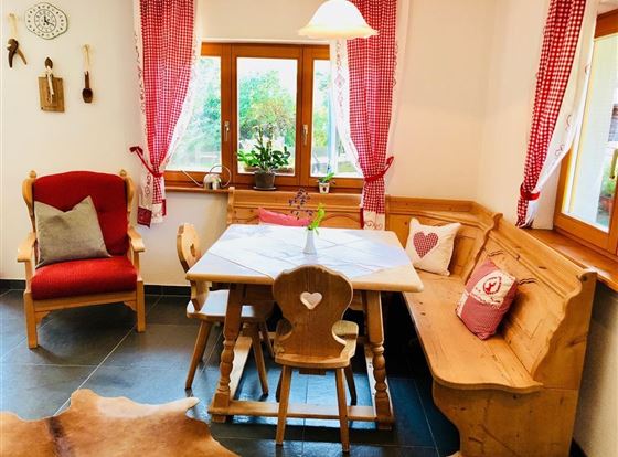 Ein gemütlicher Essbereich mit einem Holztisch und traditionellen Bänken. Rote Kissen und Vorhänge verleihen dem Raum eine einladende Atmosphäre.