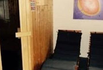 Ein gemütlicher Wellnessbereich mit einer Sauna und zwei Liegen. Die Wände sind aus Holz und ein farbiges Bild hängt an der Wand.