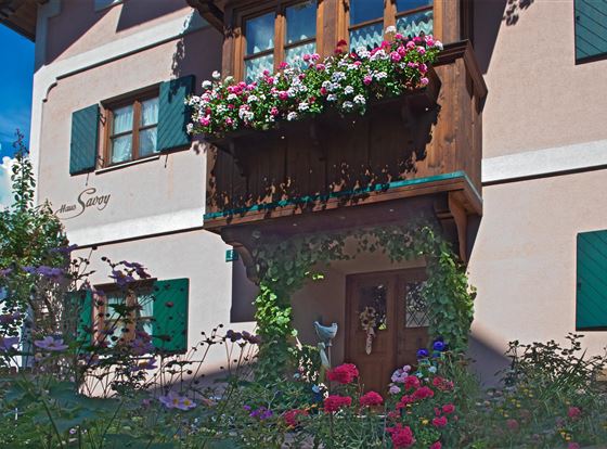 Ein charmantes Haus mit bunten Blumenkästen und blühenden Pflanzen. Die Fenster sind mit grünen Holzläden versehen und schaffen eine gemütliche Atmosphäre.