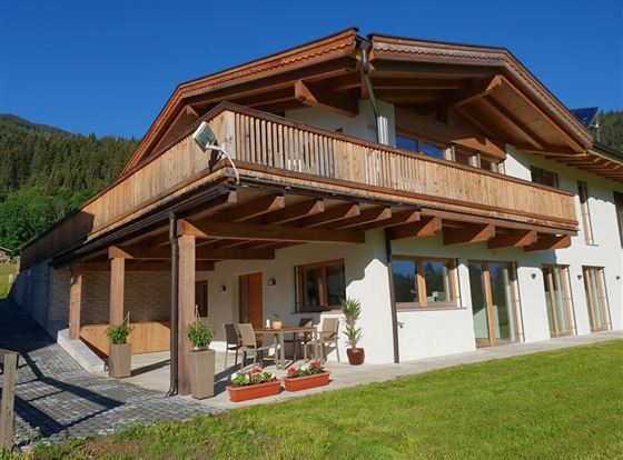 Ein modernes Haus mit Holzverkleidung und großem Balkon. Der schöne Außenbereich enthält einen Garten mit Pflanzen und Sitzgelegenheiten.