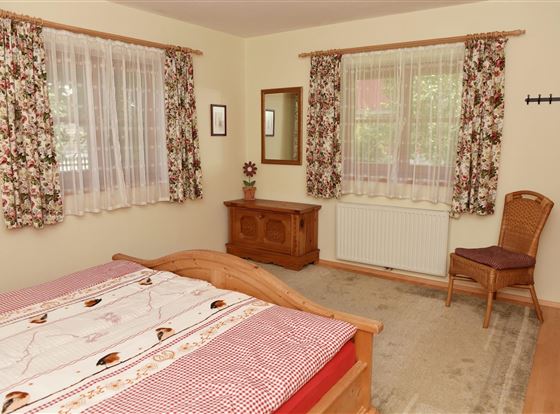 Ein gemütliches Schlafzimmer mit einem großen Bett und einem Holzschrank. Die Fenster haben florale Vorhänge und der Raum ist gut beleuchtet.