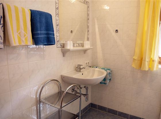 Ein helles Badezimmer mit einem Waschbecken und einem Spiegel. Gelbe Vorhänge und Handtücher verleihen dem Raum eine freundliche Atmosphäre.