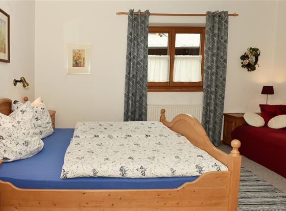 Ein gemütliches Schlafzimmer mit einem Doppelbett und zwei Kissen. Neben dem Bett befindet sich eine rote Couch und ein Fenster mit Vorhängen.