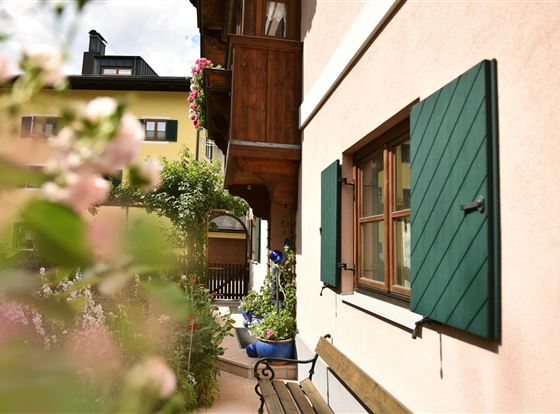 Ein charmantes Haus mit grünen Fensterläden und einer blühenden Gartenecke. Die Umgebung ist einladend und freundlich gestaltet.