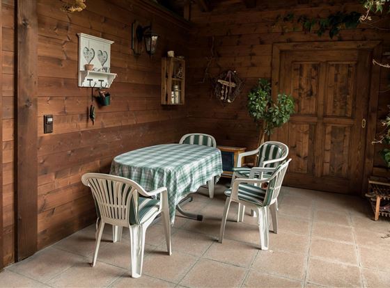 Ein gemütlicher Innenraum mit einem Tisch und Stühlen aus Kunststoff. Die Wände sind aus Holz, und es gibt ein paar Pflanzen sowie dekorative Elemente.