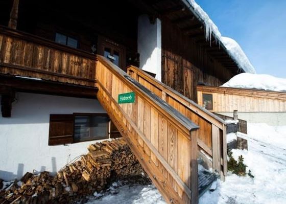 Eine gemütliche Berghütte mit Holztreppe und Schneebedecktem Dach. Der Eingang ist in einem malerischen, verschneiten Umfeld.