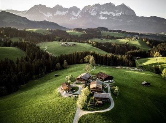 Eine malerische Landschaft mit sanften Hügeln und einem Bauernhof. Im Hintergrund erheben sich majestätische Berge.