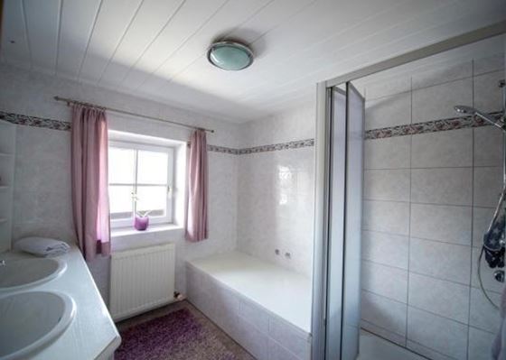 Ein helles Badezimmer mit Dusche und Badewanne. Es gibt zwei Waschbecken und Fenstervorhänge in sanften Farben.