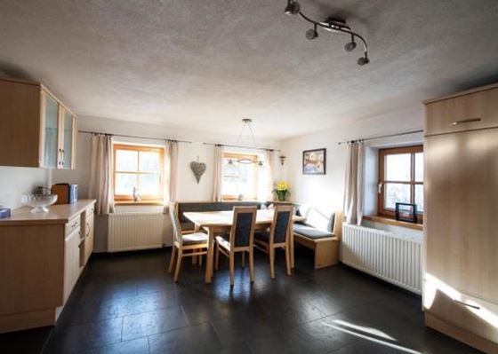 Eine helle und freundliche Küche mit einem großen Esstisch und Holzstühlen. Die Fensterscheiben lassen viel Licht herein und bieten einen Blick nach draußen.