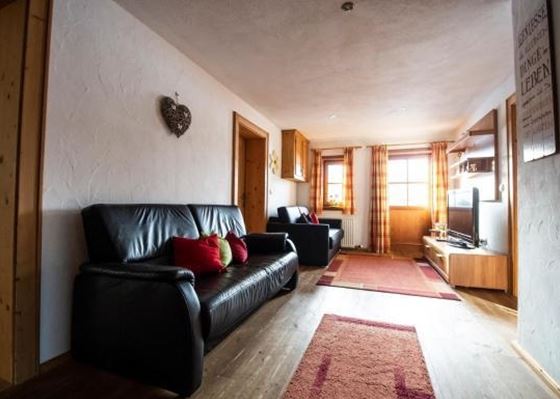 Ein gemütlicher Wohnraum mit zwei Sofas und einem Fernseher. Große Fenster sorgen für viel Licht und eine einladende Atmosphäre.