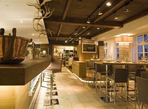 Ein stilvolles Restaurant mit modernem Interieur und warmem Licht. Die Bar ist mit eleganten Hochstühlen und einem offenen Bereich für das Essen ausgestattet.