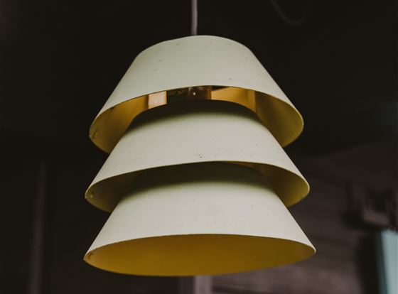 Eine stilvolle Hängeleuchte mit mehreren Schichten in sanften Grüntönen. Sie hängt in einem dunklen Raum und bringt modernes Design in die Umgebung.