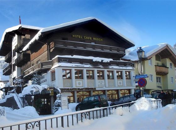 Ein charmantes Hotel mit dem Namen "Hotel Café Brech" im Schnee. Die umliegenden Berge und das klare, blaue Himmel schaffen eine idyllische Winteratmosphäre.