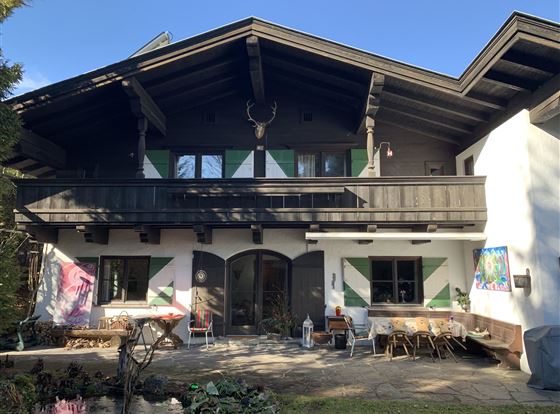 Ein traditionelles Alpenhaus mit einem schönen Balkon und bunten Fenstern. Der Außenbereich ist mit Stühlen und Tischen zum Entspannen ausgestattet.