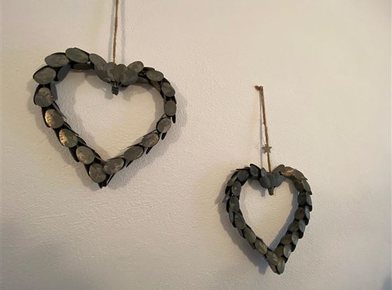 Zwei hängende Herzdekorationen aus Holz, die an einer Wand befestigt sind. Die Herzen sind aus dunklen Holzscheiben gefertigt und verleihen einen rustikalen Charme.